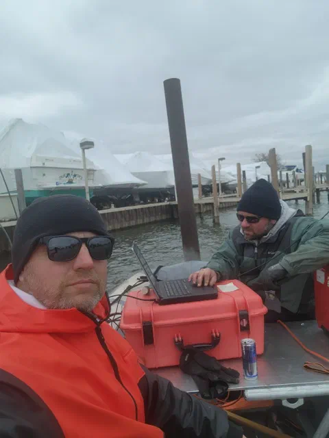 Harrison and Chris on a survey boat at a marina, running a laptop on a rugged case on deck